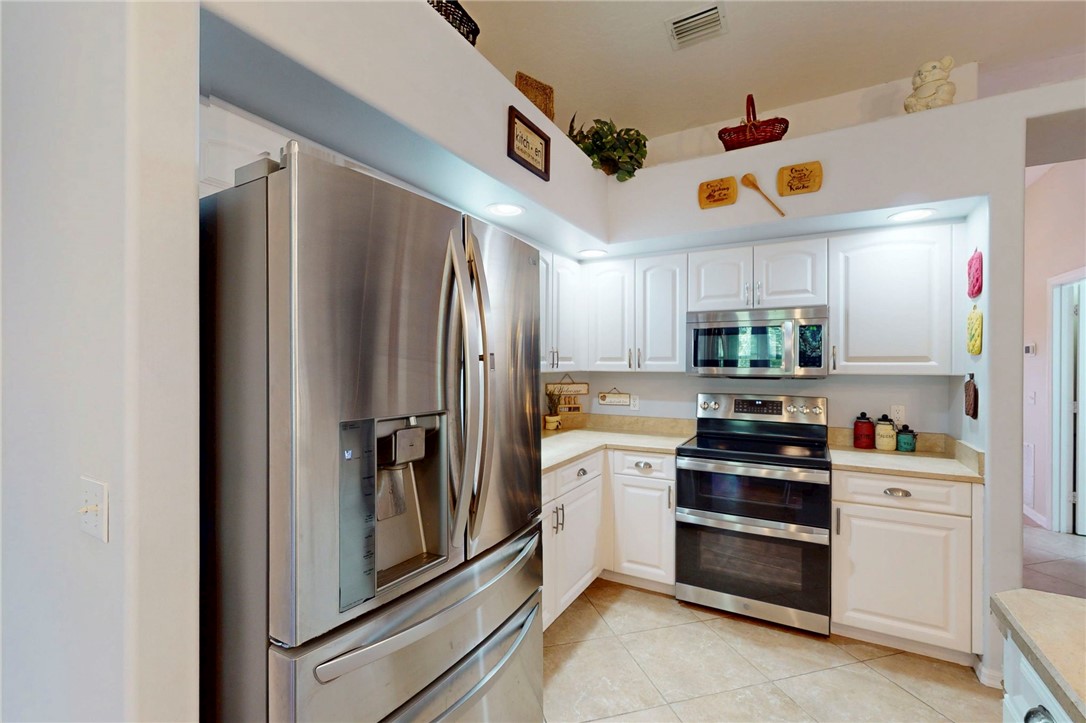 Kitchen featuring white raised-panel cabinetry, stainless steel French-door refrigerator, integrated over-the-range microwave, stainless steel range with double oven, and tile flooring