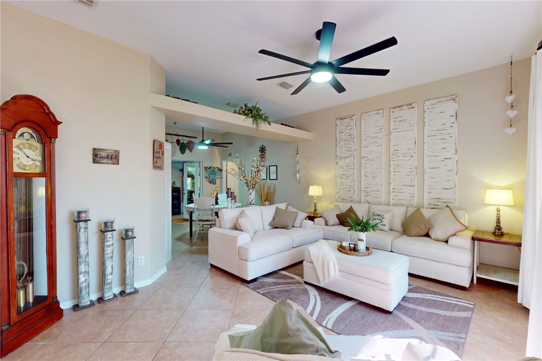 Living area featuring neutral tile flooring, high ceilings with an integrated architectural niche, and a multi-blade ceiling fan with centered light fixture