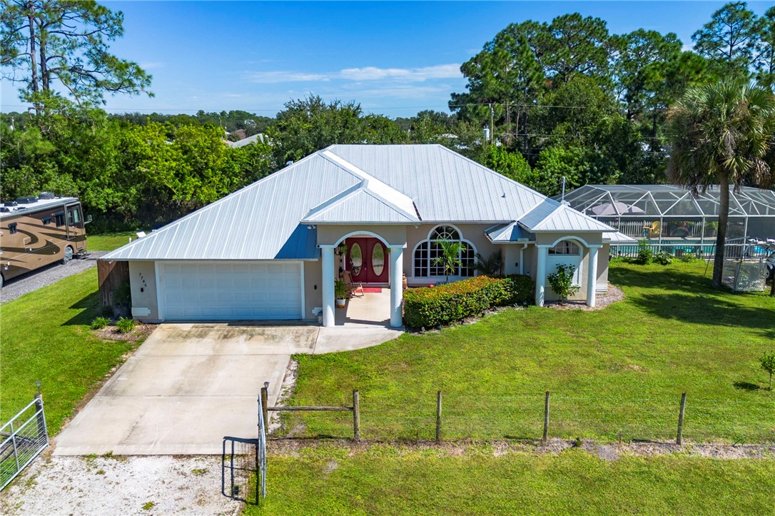 Single-story residence featuring a metal roof, arched double-door entry, covered portico with dual columns, two-car garage, and a screened-in swimming pool enclosure