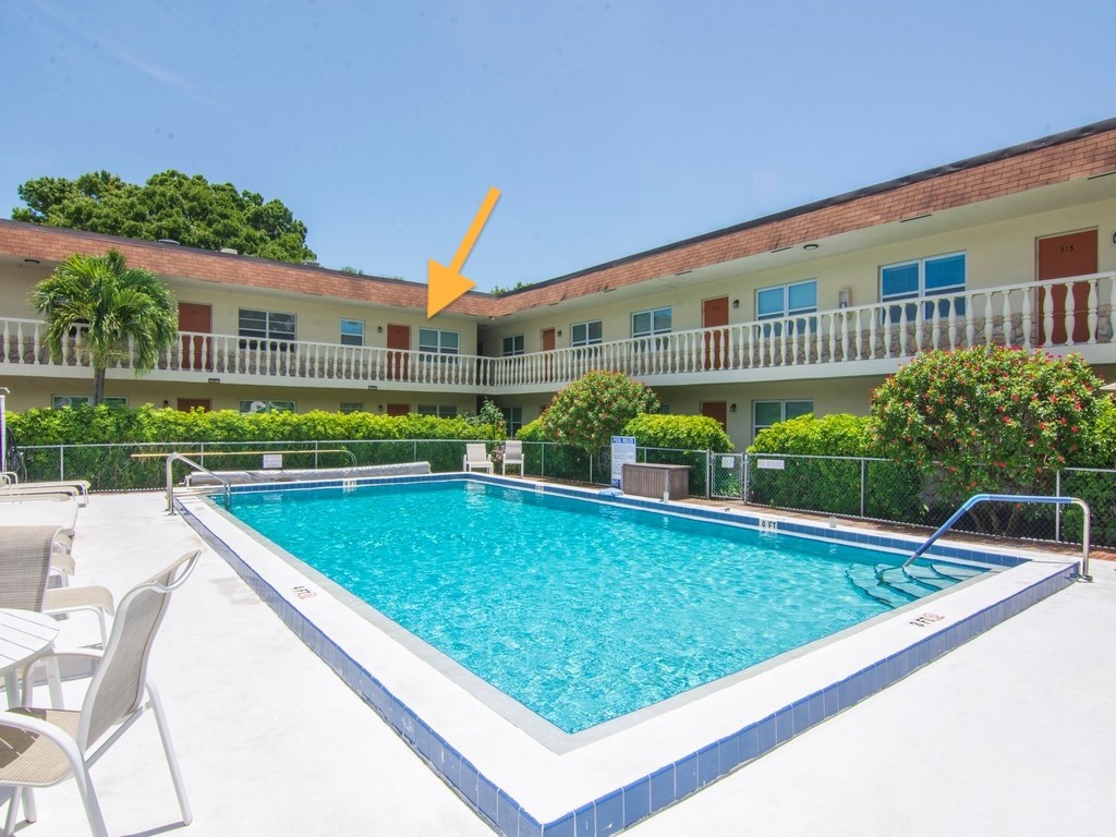Outdoor swimming pool featuring a tiled perimeter and metal handrails, set within a courtyard area with perimeter fencing and landscaping