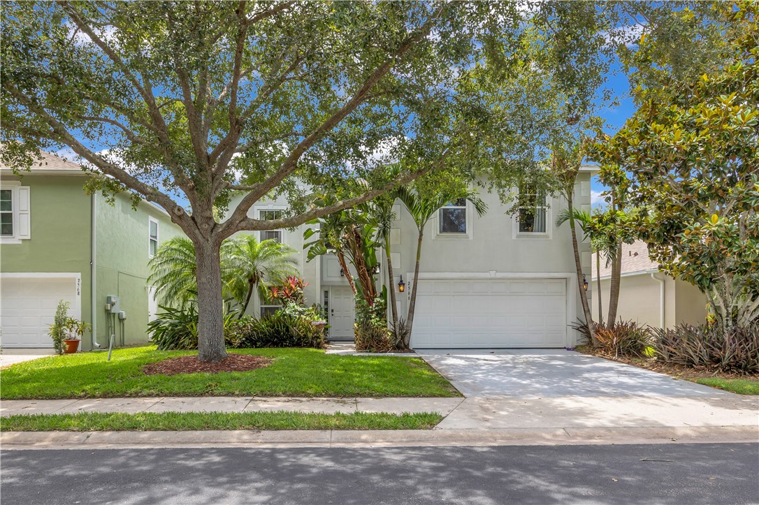 Two-story exterior featuring a stucco facade, attached two-car garage, concrete driveway, and mature landscaping