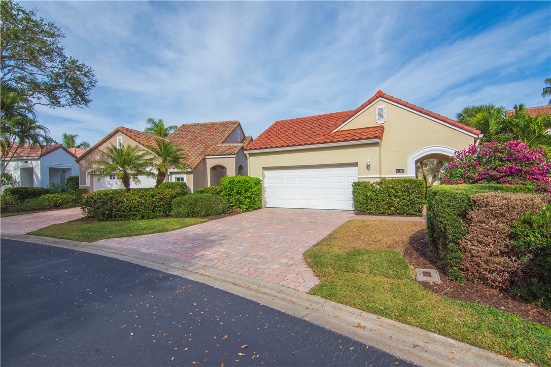 Mediterranean-style exterior featuring a terracotta tile roof, paver driveway, two-car garage, and manicured landscaping
