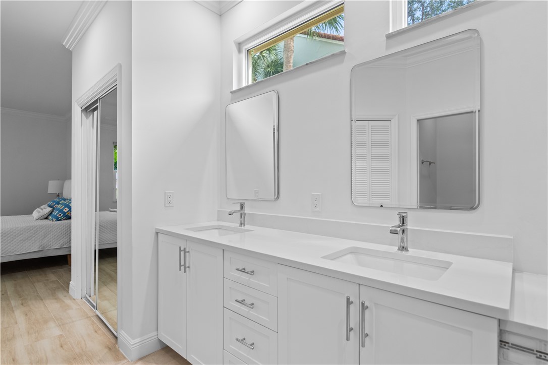 Dual-sink vanity with white cabinetry, light-toned countertop, rectangular undermount basins, and chrome fixtures, complemented by wall-mounted mirrors and an overhead transom window