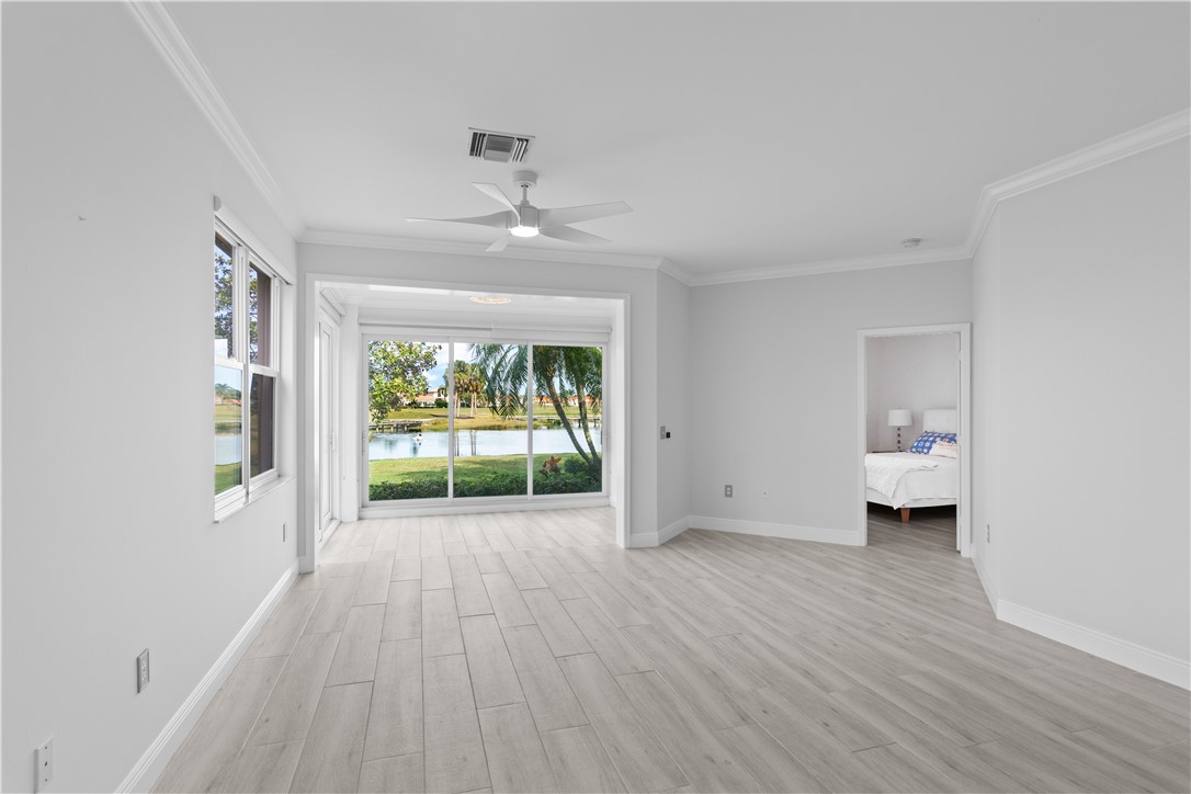 Living space featuring light-toned wood-finish flooring, crown molding, a ceiling fan, and floor-to-ceiling sliding glass doors offering water and landscape scenery
