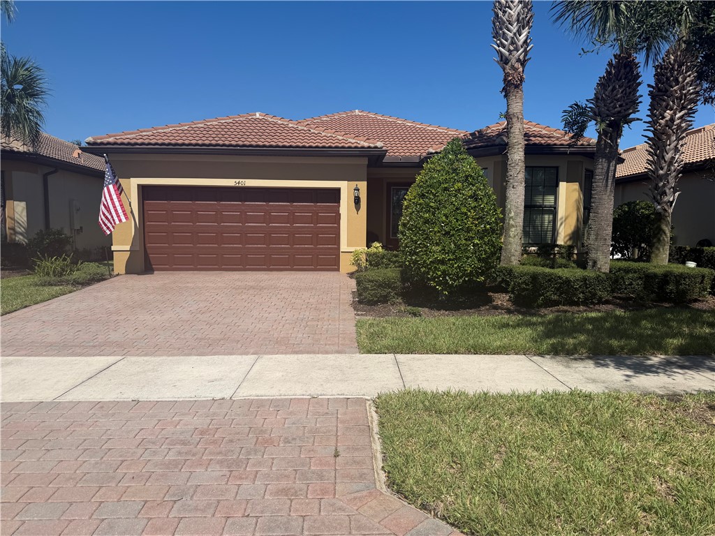 Stucco exterior featuring a tiled roof, multi-car garage, and brick-paver driveway surrounded by manicured landscaping
