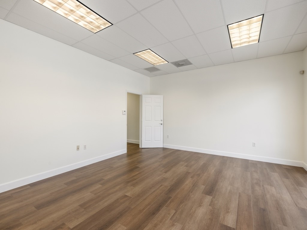 Wood-finish flooring, white walls, and a suspended ceiling with integrated lighting