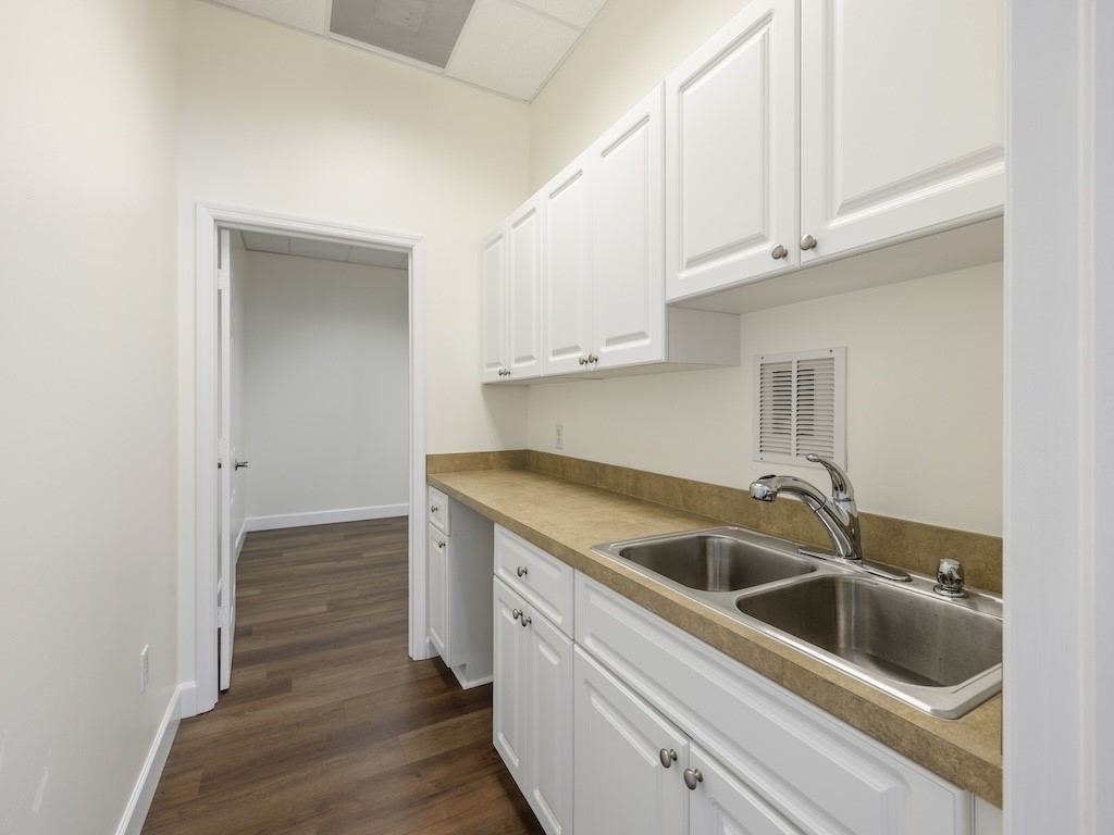 Wood-finish flooring, white cabinetry with silver-tone hardware, a double-basin stainless steel sink, and a laminate countertop