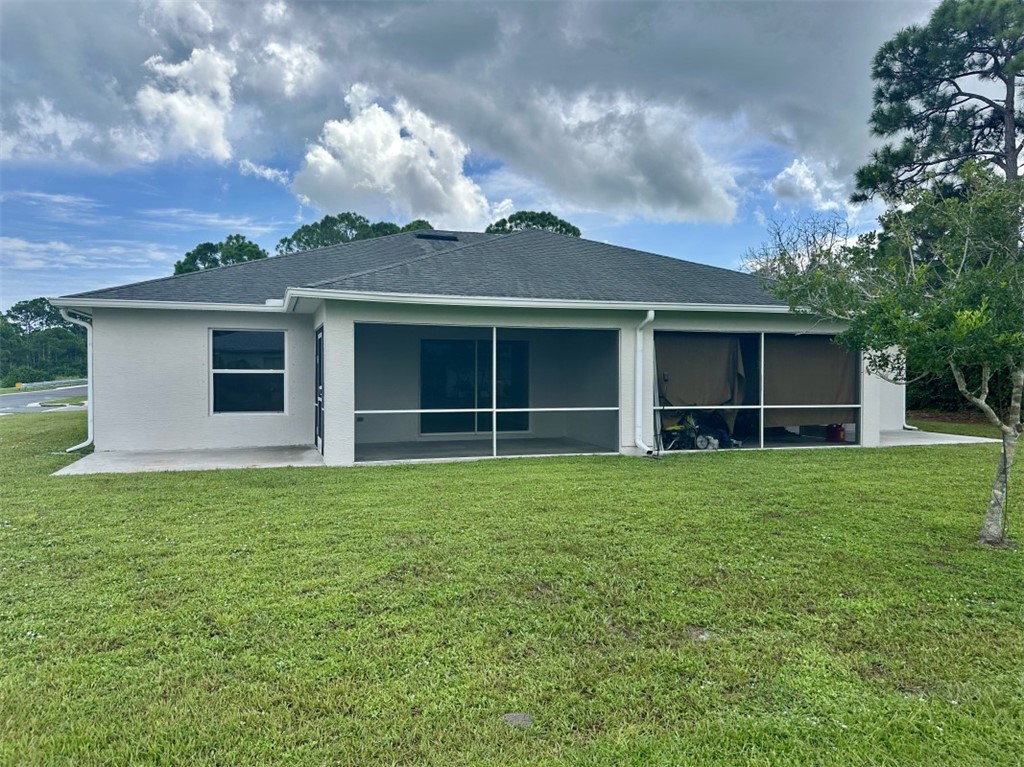 Rear exterior with a screened lanai, concrete patio, and mature landscaping