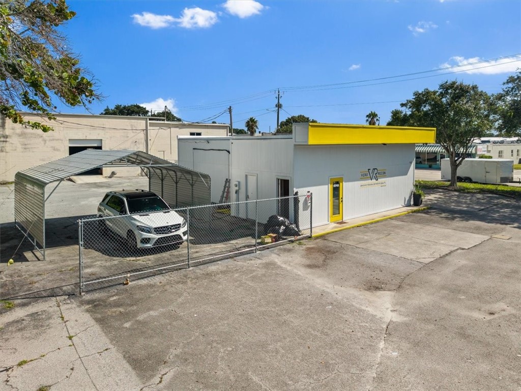 Commercial building with a bright yellow fascia and door, corrugated metal carports, and a chain-link fence