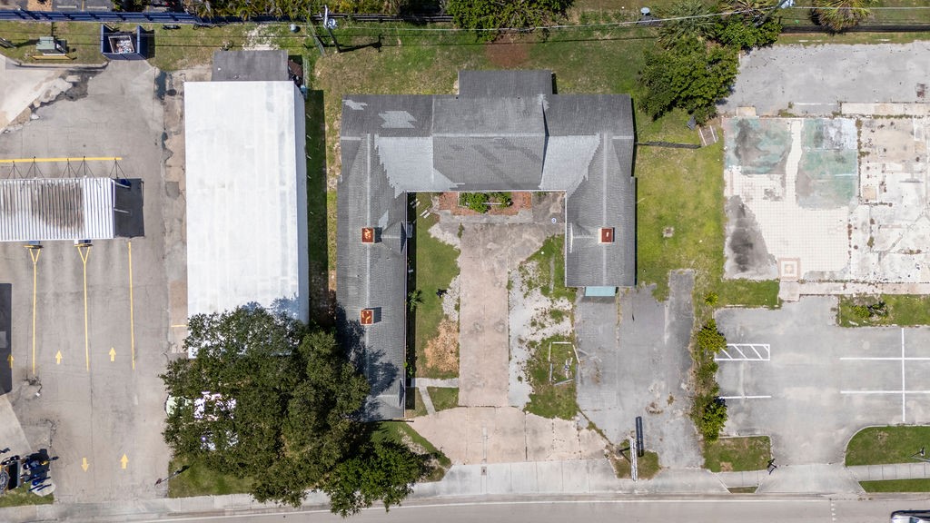 U-shaped building featuring a gray shingle roof and multiple chimneys, situated on a lot with a paved driveway and surrounding paved areas