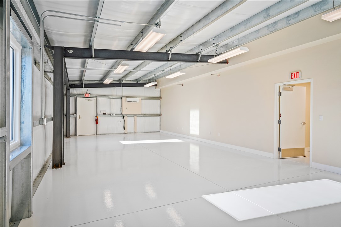 Spacious industrial-style interior featuring a polished concrete floor, exposed metal beam ceiling, multiple fluorescent light fixtures, and a large window