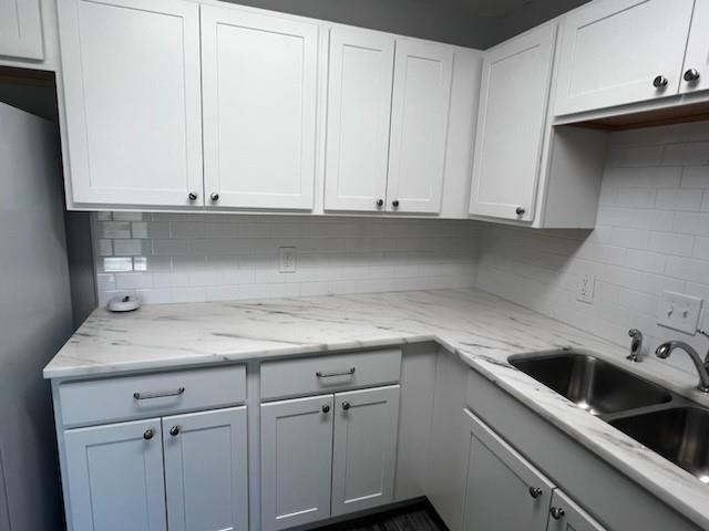 Kitchen featuring white shaker-style cabinetry with dark hardware, white subway tile backsplash, and light-toned, veined countertops