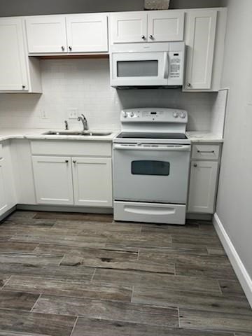 Kitchen featuring white cabinetry, white subway tile backsplash, light-toned countertops, wood-finish flooring, and white appliances including a range and microwave