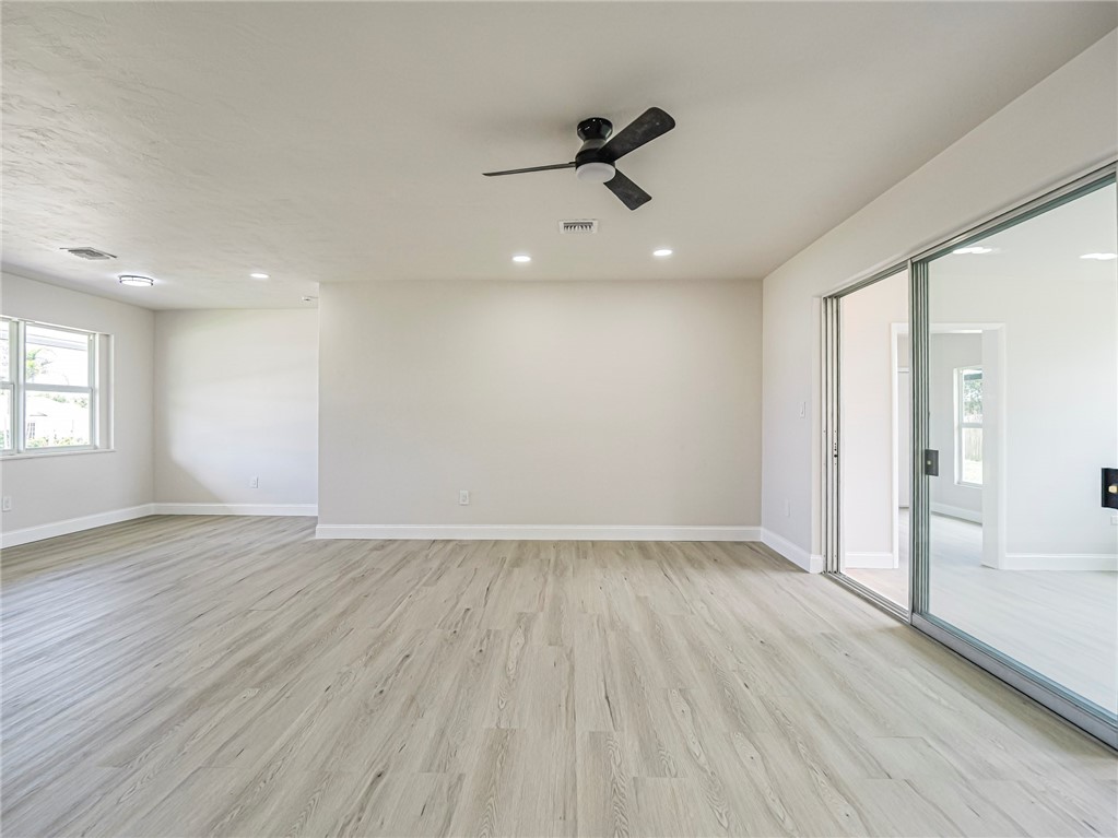 Neutral-toned living space featuring wood-finish flooring, recessed lighting, a modern ceiling fan, and large glass sliding doors