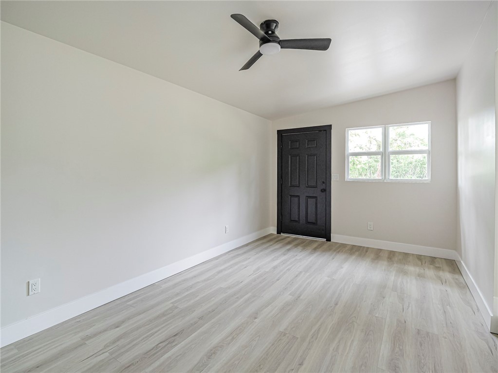 Neutral interior featuring wood-finish flooring, a matte black six-panel entry door, and a modern ceiling fan with integrated lighting