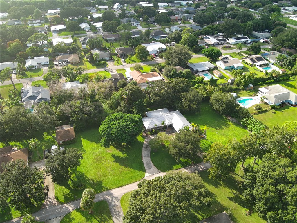 Aerial perspective of a sprawling corner lot featuring mature trees, a long concrete driveway, and extensive grass coverage