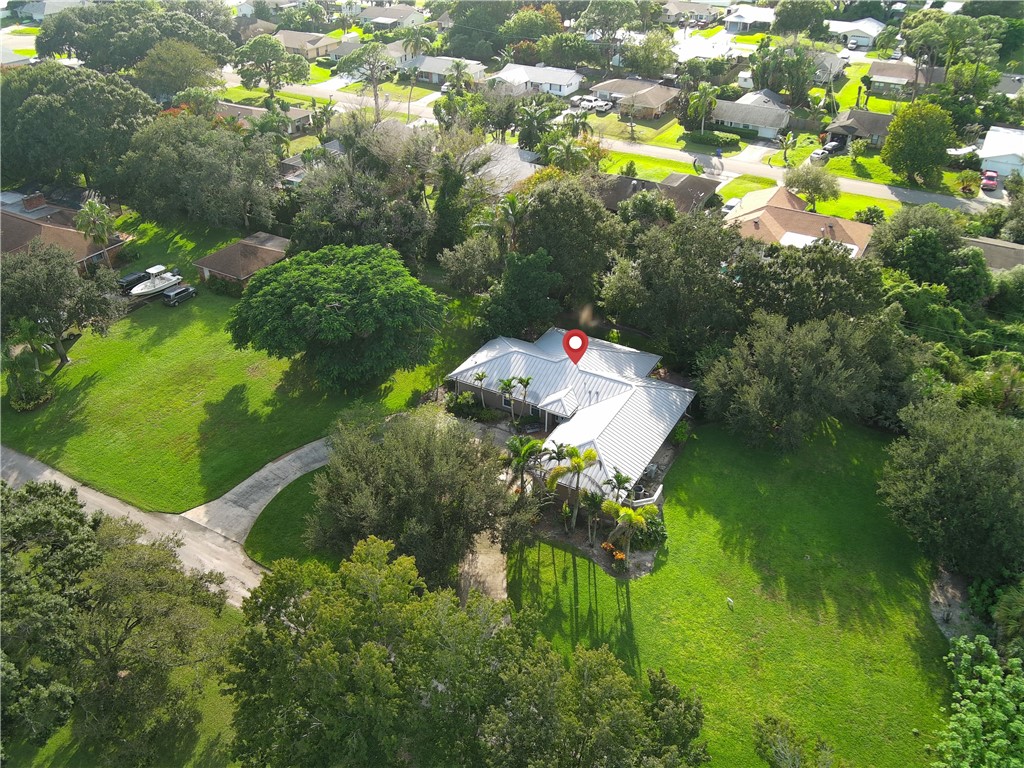 Aerial perspective of a property featuring a metal roof, expansive grounds, mature trees, and a paved driveway