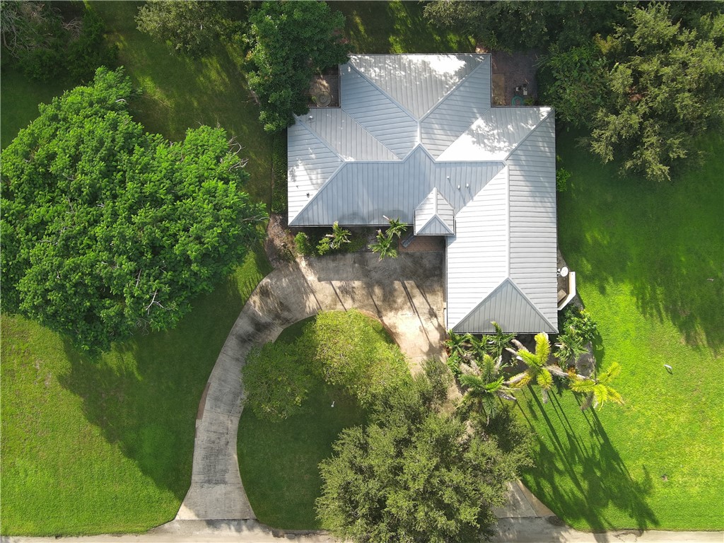 Aerial perspective featuring a metal roof system, curved concrete driveway, and expansive grounds with mature trees