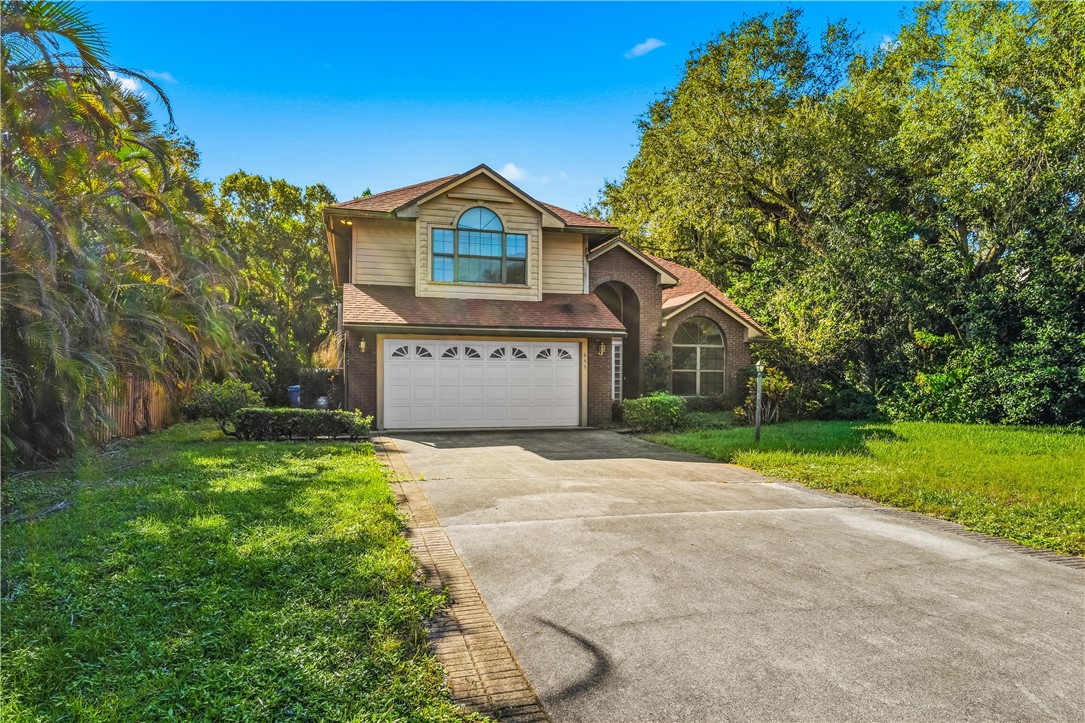 Two-story residence featuring a brick and horizontal siding exterior, arched multi-light windows, and a paved driveway leading to a two-car garage