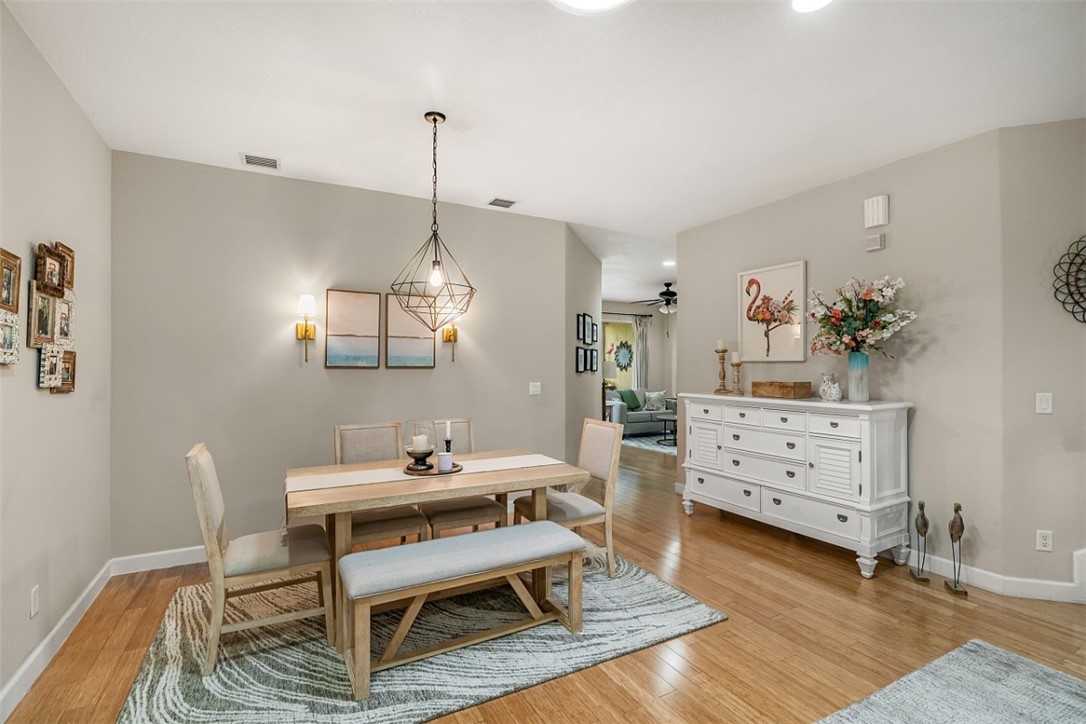 Open-concept dining area featuring wood-finish flooring, a geometric metal pendant light, and dual wall-mounted sconces
