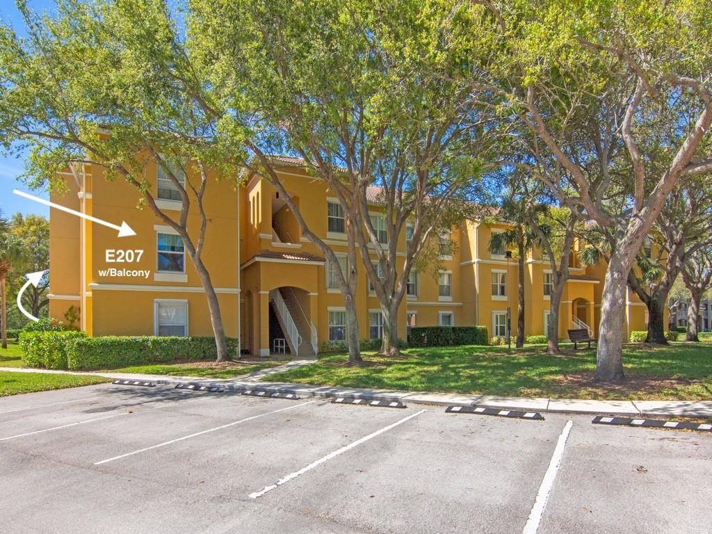 Multi-story building featuring stucco exterior, private balcony, and surrounding mature landscaping