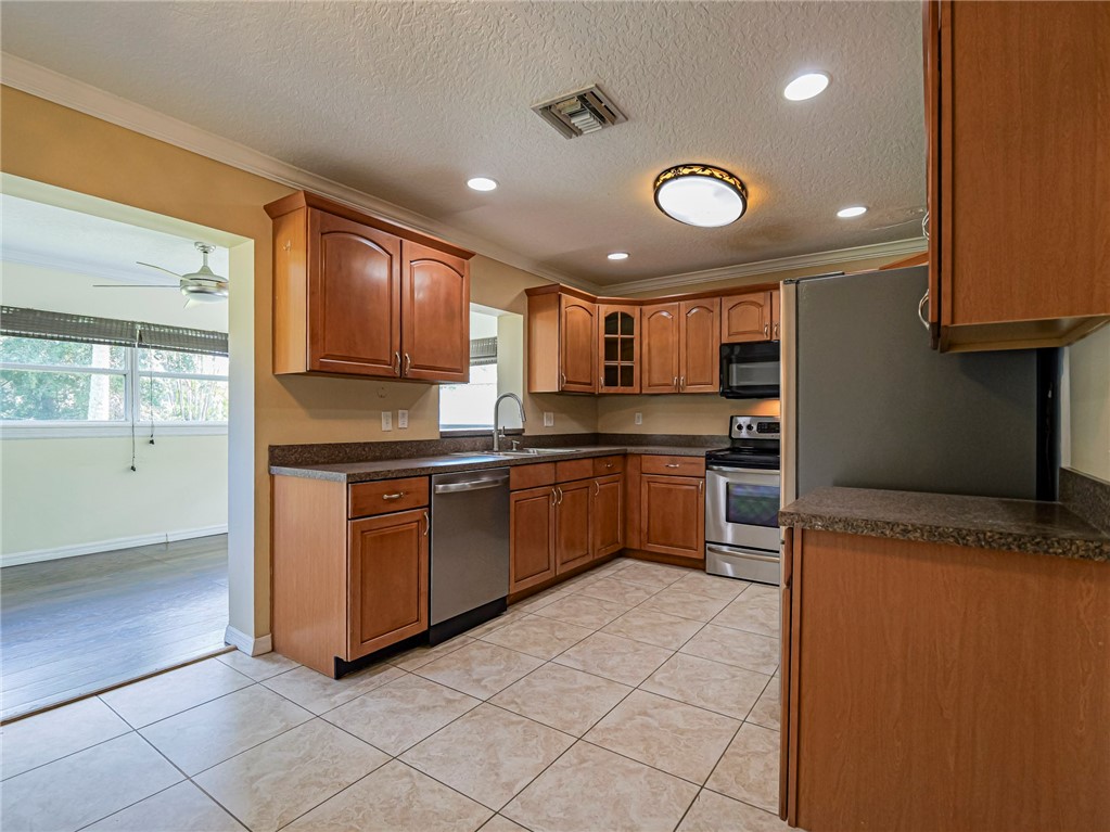 Kitchen featuring wood cabinetry, stainless steel appliances, tile flooring, stone-finish countertops, and recessed lighting