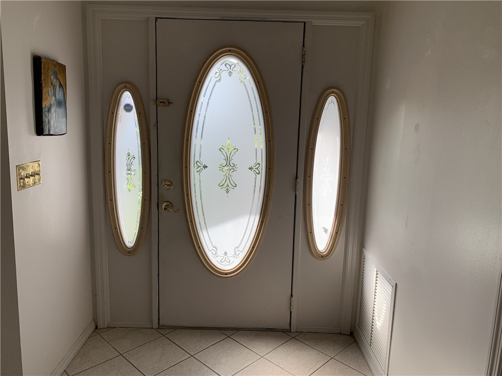Entry door featuring oval decorative glass inserts with frosted detailing, complemented by matching oval sidelights and polished metallic hardware, set against ceramic tile flooring