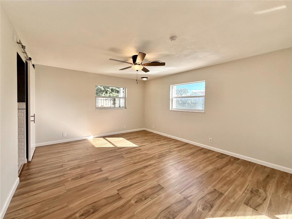 Room interior featuring wood-finish flooring, two dual-pane windows, a ceiling fan with light fixture, and a sliding barn-style door