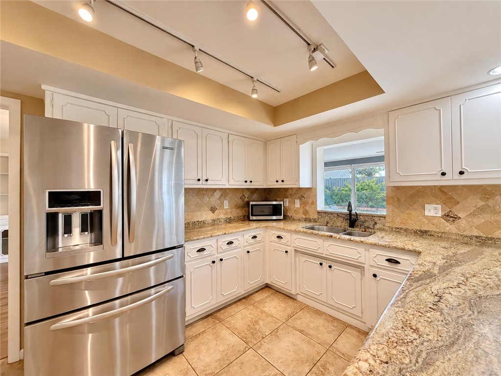 Kitchen featuring white raised-panel cabinetry, light stone countertops, diagonal stone tile backsplash, stainless steel refrigerator, and recessed track lighting