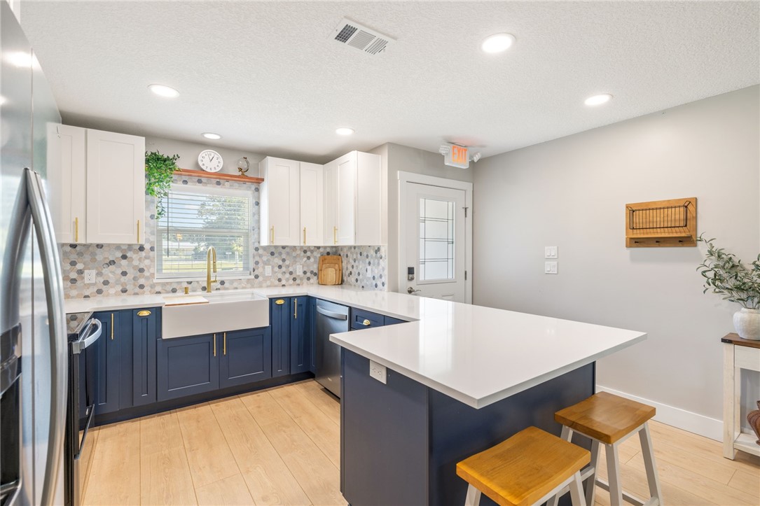 Kitchen featuring two-tone cabinetry, quartz countertops, hexagonal mosaic tile backsplash, apron-front sink, and wood-finish flooring