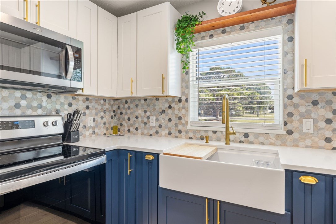 Kitchen featuring white upper cabinetry, blue lower cabinetry, brass hardware, apron-front farmhouse sink, and a multi-tone hexagonal tile backsplash