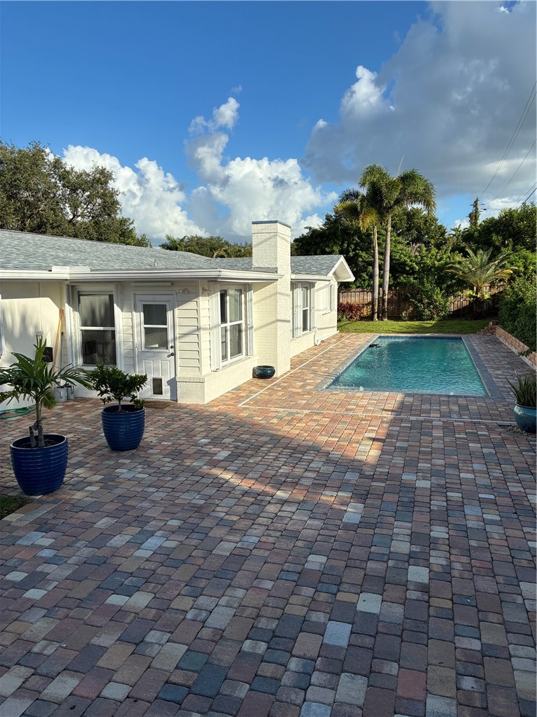 In-ground swimming pool, expansive paver patio, exterior masonry chimney, and light-toned lap siding