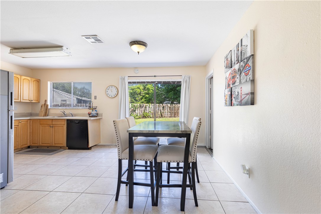 Kitchen featuring wood cabinetry, ceramic tile flooring, and integrated black dishwasher, with sliding glass doors opening to the exterior