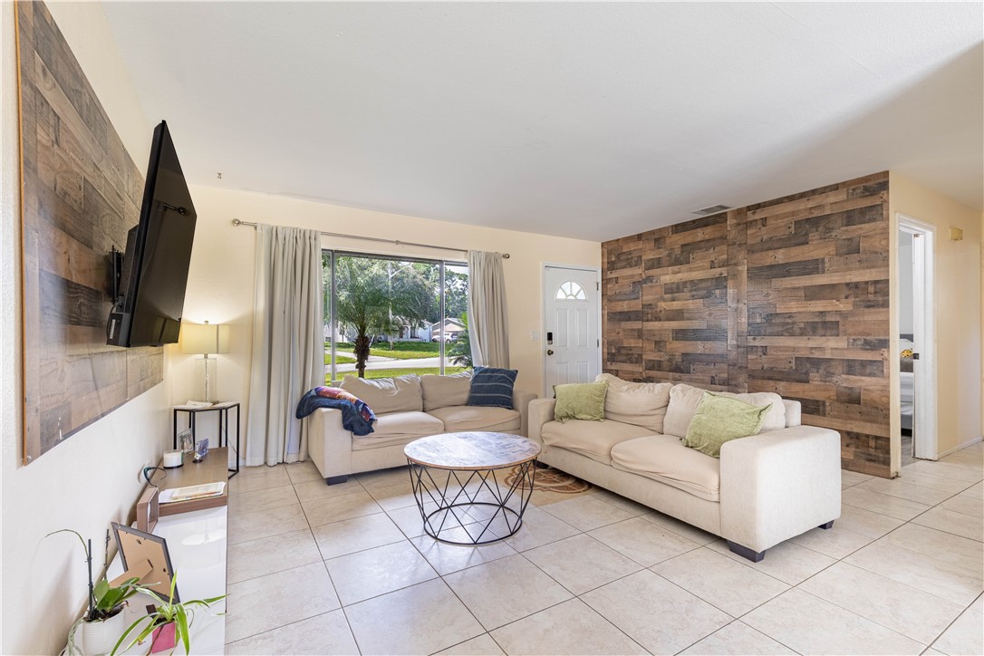 Living space featuring neutral ceramic tile flooring, wood-plank accent walls, and large window with exterior natural light
