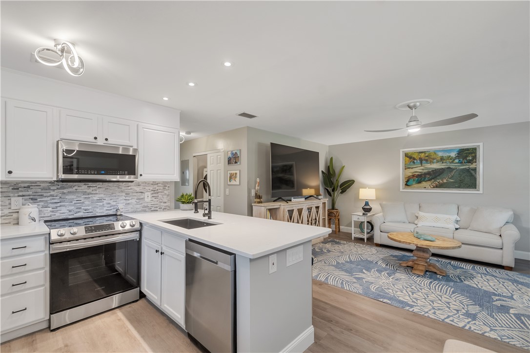 Kitchen featuring white cabinetry, solid-surface countertops, stainless steel appliances, multi-toned tile backsplash, and wood-finish flooring
