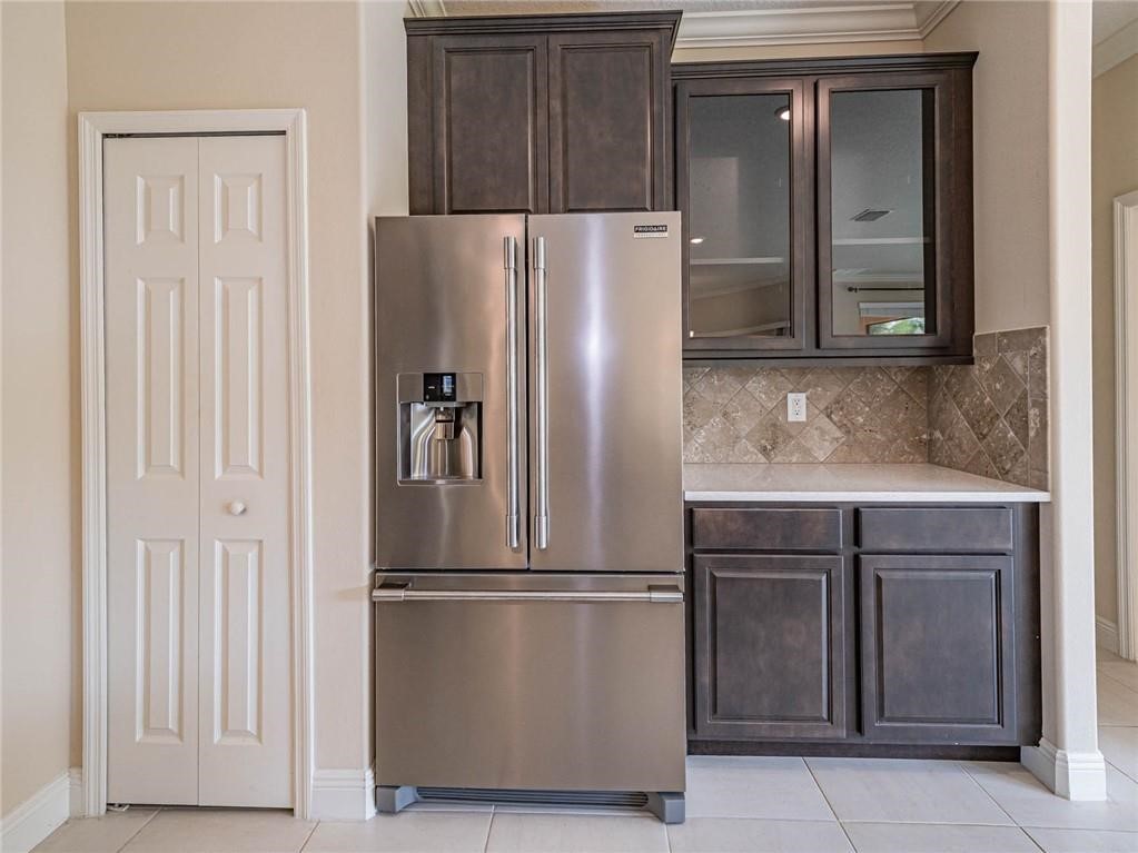 Kitchen with stainless steel fridge with ice dispenser, glass insert cabinets, light tile patterned floors, dark brown cabinets, and light stone countertops