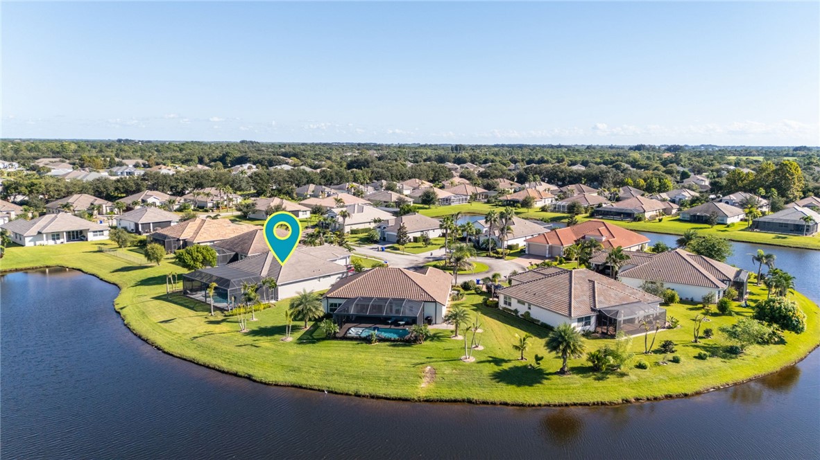 Aerial perspective of residential property featuring waterfront positioning, screened-in swimming pool, hip roof architecture, and perimeter landscaping