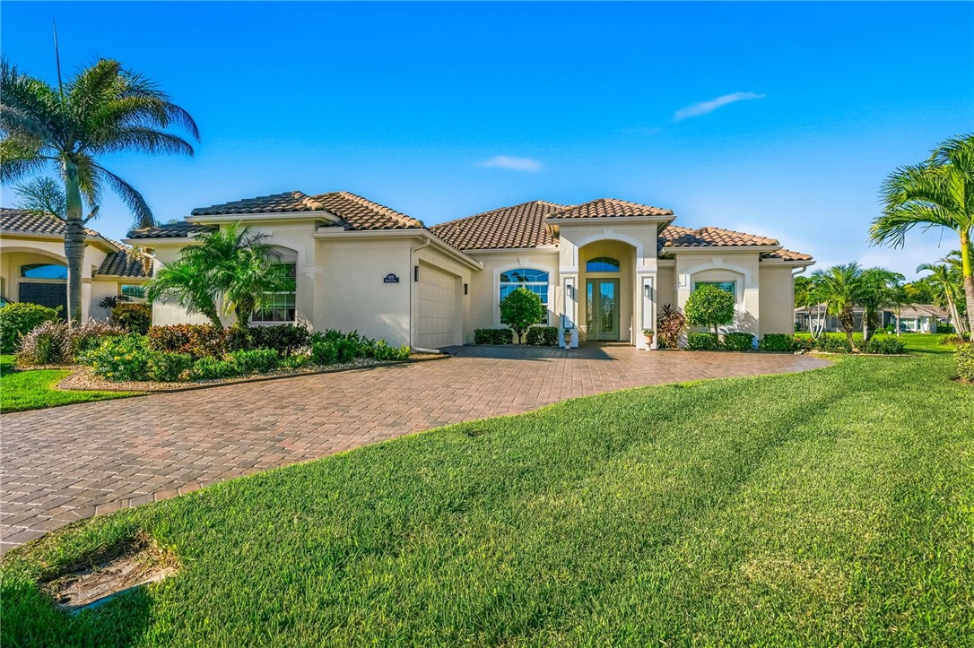 Stucco exterior featuring a tiled roof, arched entryway, paved driveway, and established palm landscaping