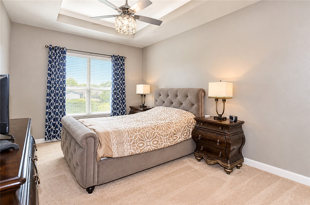 Bedroom featuring a tray ceiling, central ceiling fan with integrated lighting, neutral wall paint, and wall-to-wall carpeting