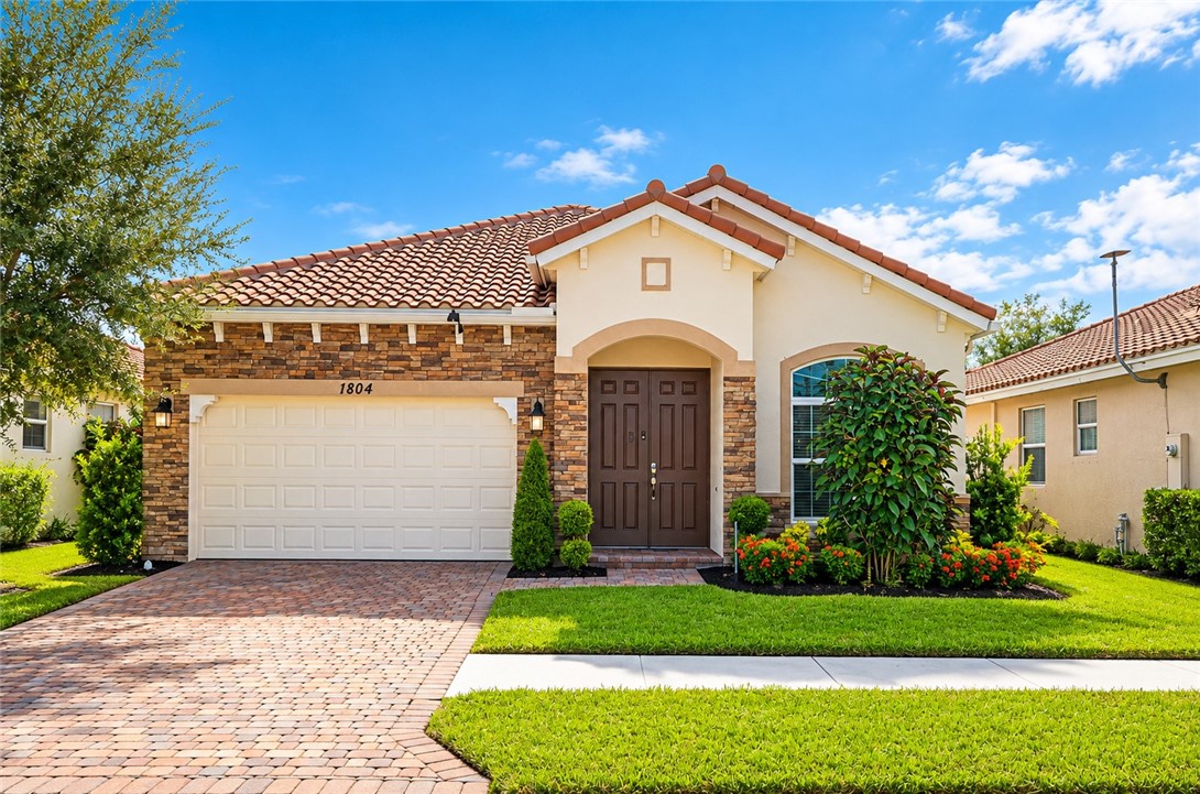 Single-story exterior featuring a stone veneer facade, tile roof, brick-paver driveway, and double entry doors