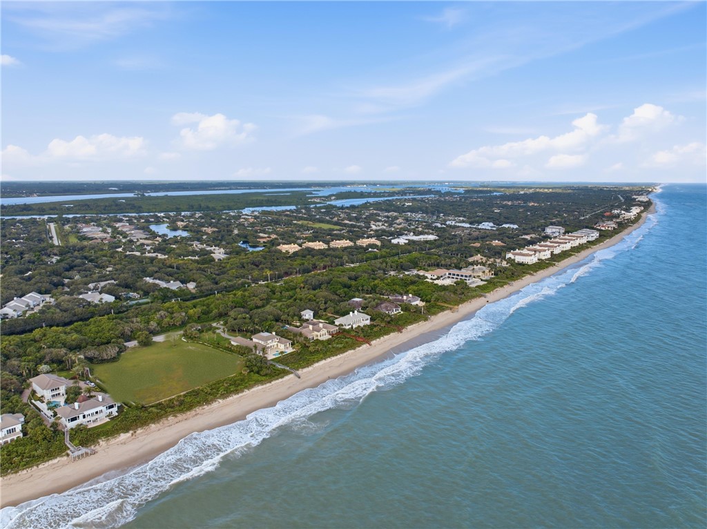 Coastal aerial perspective featuring direct oceanfront access, sandy shoreline, and mature tree canopy