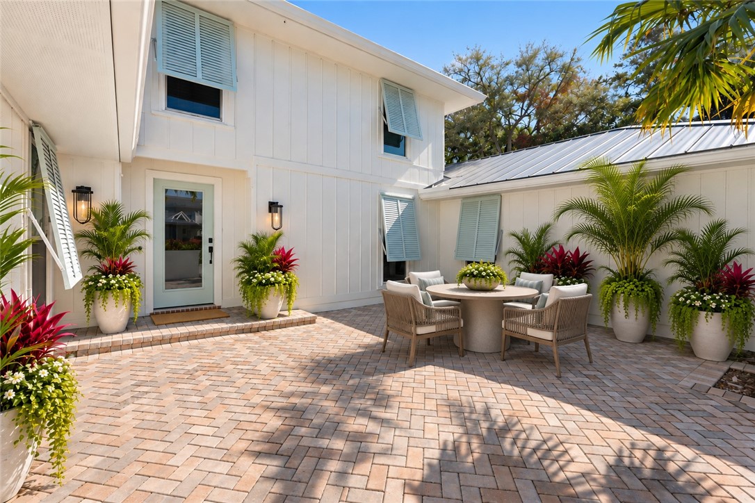 Virtually Staged - Courtyard featuring herringbone-patterned paver flooring, board-and-batten siding, metal roof accents, and exterior wall-mounted lanterns