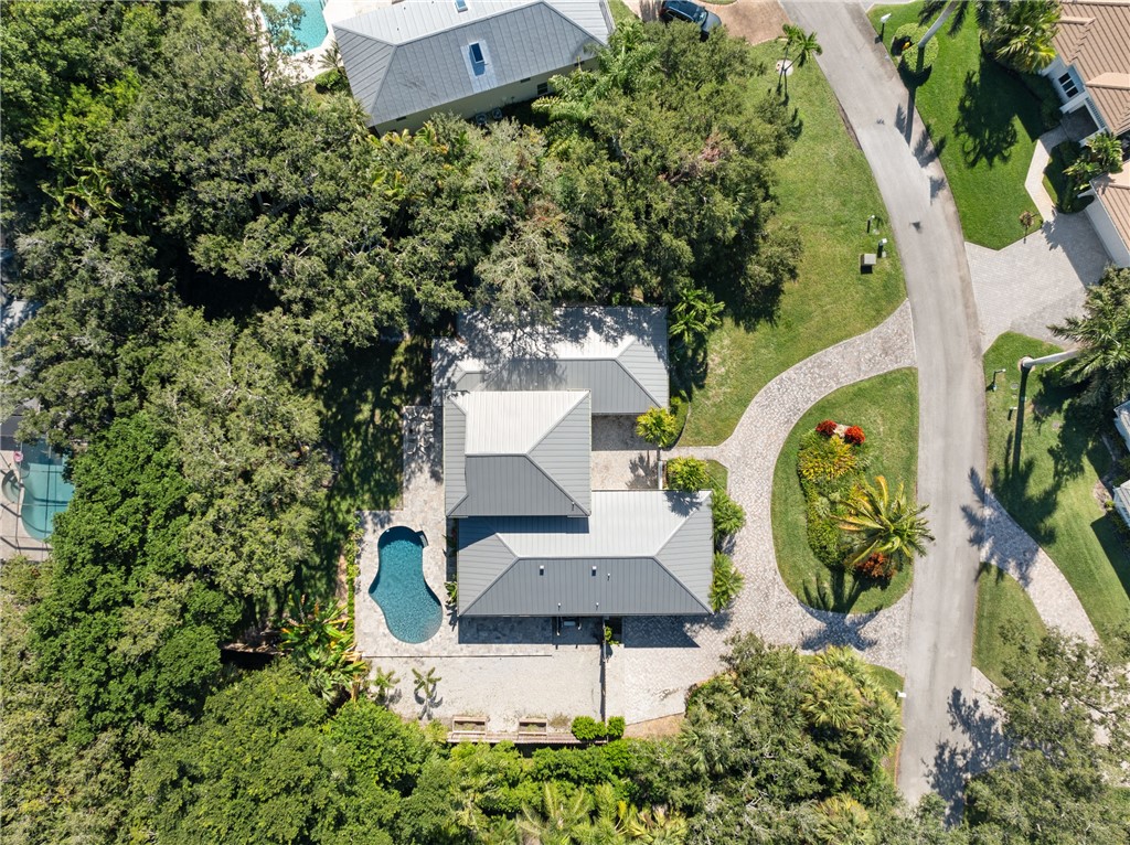 Aerial view of residential property featuring a metal roof, paved driveway, swimming pool, and mature landscape
