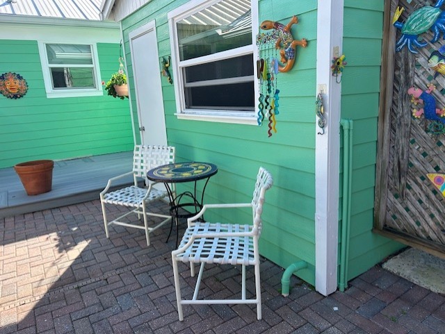 Exterior space featuring horizontal lap siding, a brick paver patio, and a raised composite deck with a window
