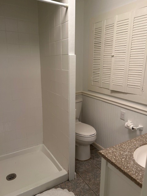 Shower stall with white tile surround, beadboard wainscoting, louvered window shutters, speckled solid-surface vanity countertop, and tile flooring