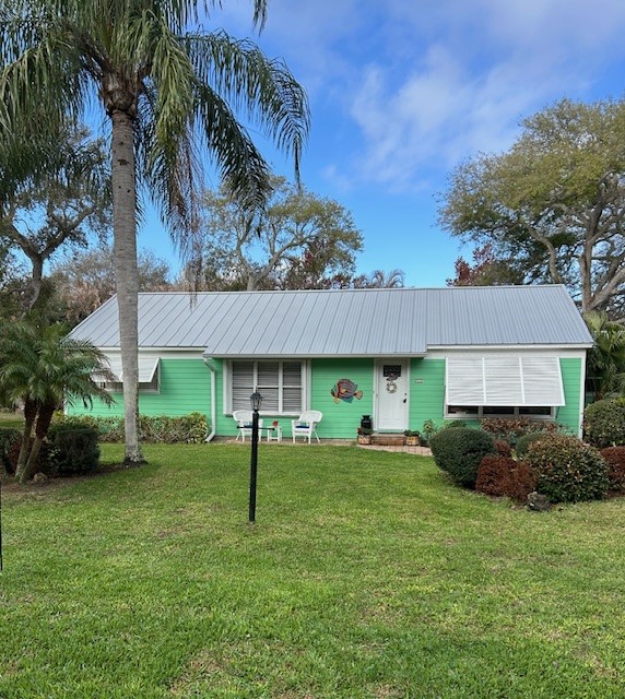 Single-story residence featuring a metal roof, horizontal lap siding, retractable window shutters, and mature landscaping