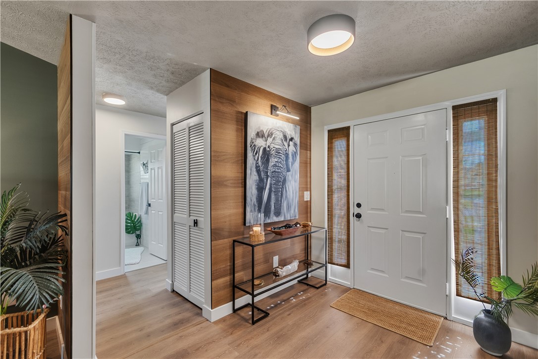 Entryway featuring wood-finish accent wall paneling, wood-finish flooring, white paneled entry door with sidelights, and modern flush-mount lighting fixtures