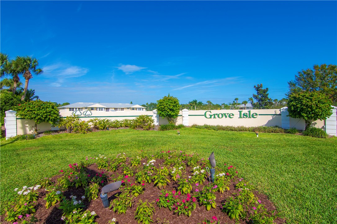 Grove Isle entrance signage featuring a decorative masonry wall, manicured lawn, formal landscape beds, and mature palm trees