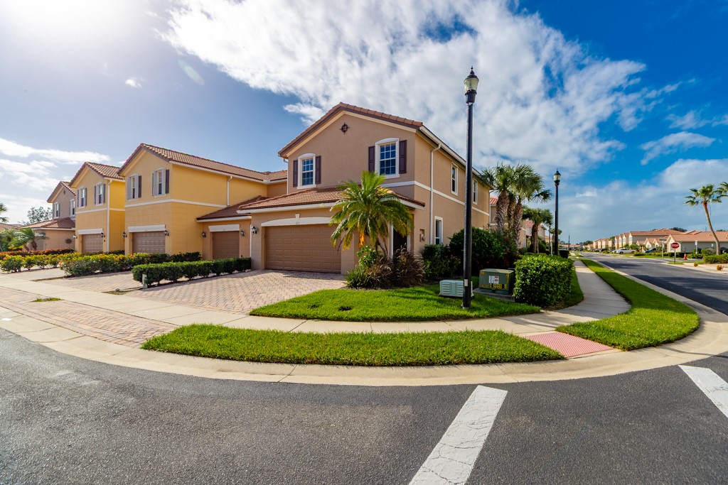 Two-story stucco exterior featuring a tiled roof, attached two-car garage, and paver driveway, situated on a corner lot with landscaped grounds