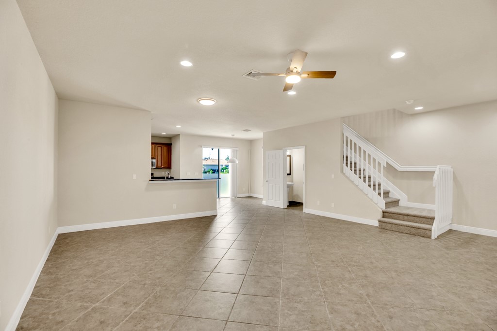 Open living area featuring large-format tile flooring, recessed lighting, a ceiling fan, a kitchen peninsula, and a staircase with a white balustrade